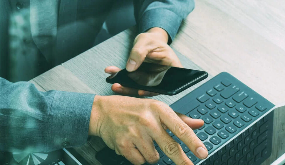Homem que digita em um smartphone enquanto toca na tela de um notebook