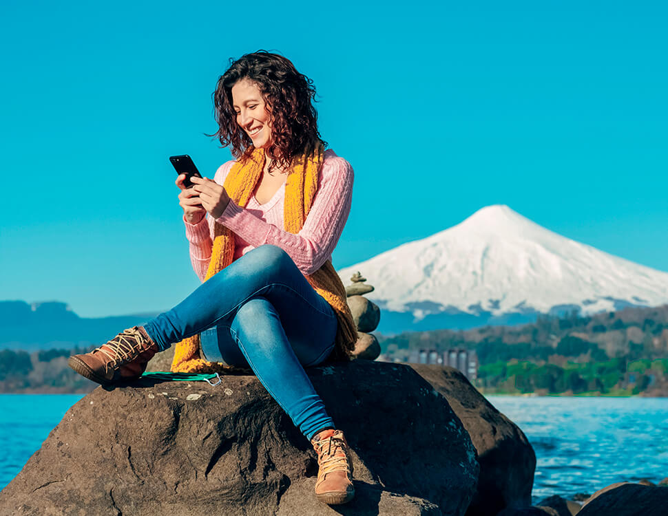 Mulher que está sentada em uma pedra digitando em um smartphone